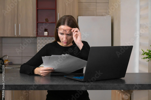 Obraz na płótnie Stunned woman working from home, raising her glasses while reading documents, displaying a shocked expression as she processes unexpected financial news and bills w salonie