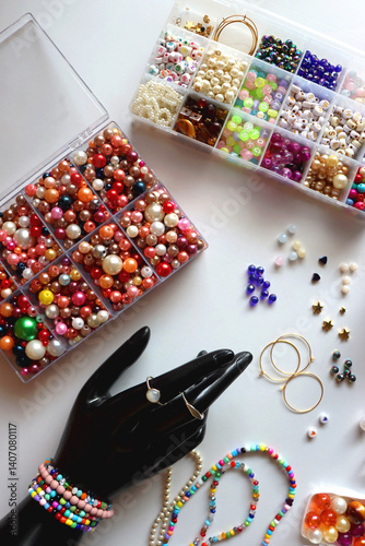 Hand figurine, colorful friendship bracelets, necklaces, various beads and DIY supplies on the table. Making jewelry at home. Flat lay.