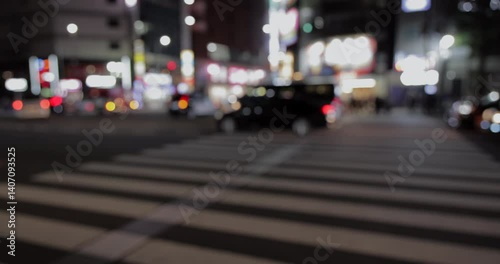 Out of focus night scene of traffic and crosswalk in Tokyo with cars moving under bright city lights and urban glow in a blurred frame