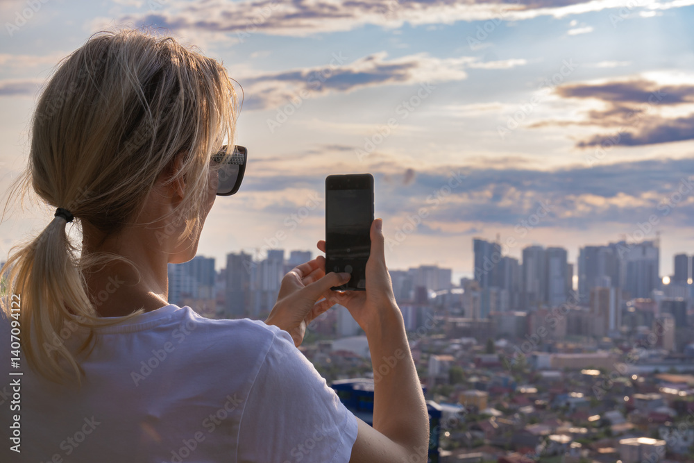 Young woman filming an urban landscape at sunset from her smartphone, enjoying the beauty of urban architecture and sharing her adventures on social networks.
