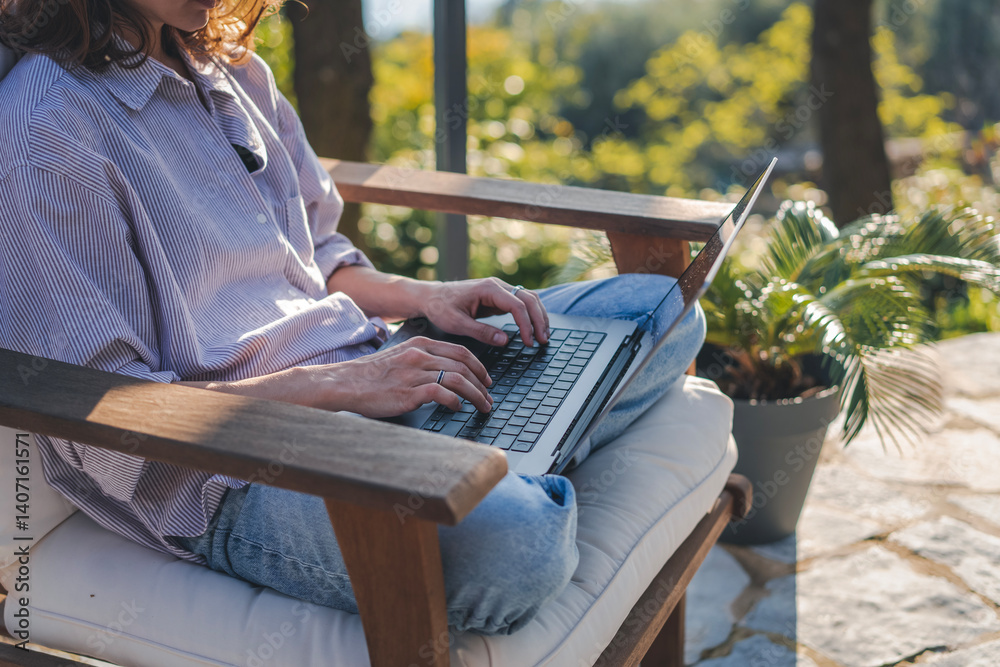 Young woman sitting on cottage terrace using laptop in summertime, online work