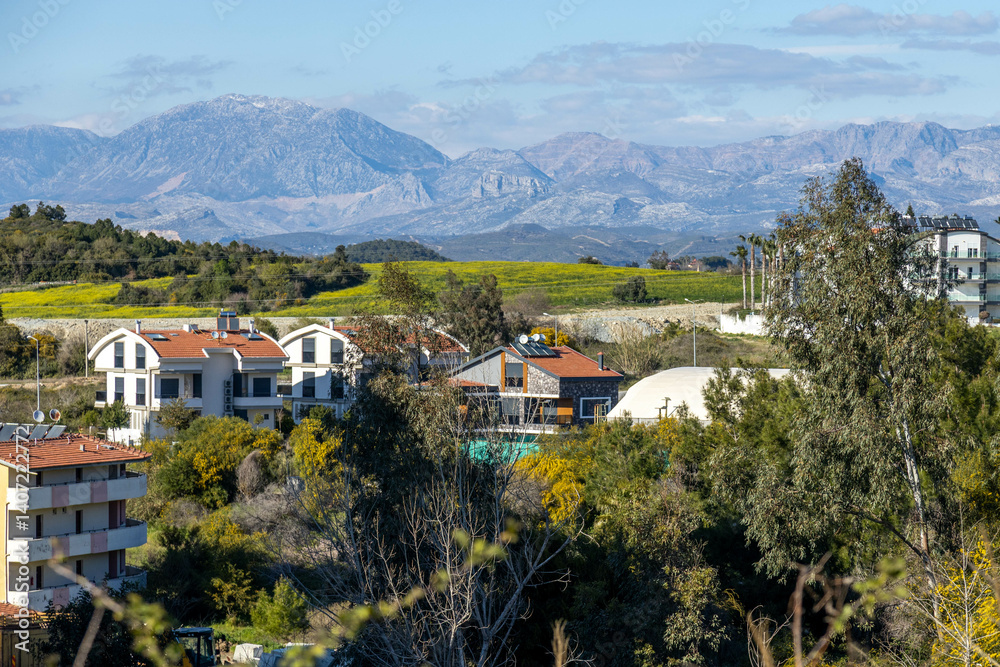 Obraz premium Peaceful spring view of Ilıca village with modern houses and mountain backdrop under a clear sky. Ilıca, Antalya, Turkey.