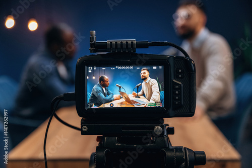 Close up view of camera that is filming. Two radio presenters recording an audio broadcast in a studio photo