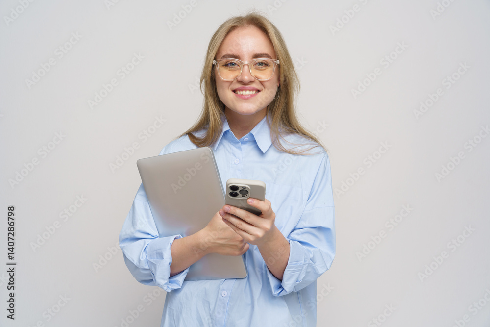 Young Woman Smiling With a Tablet and Phone, Dressed Casually in a Light Blue Shirt, Exuding Confidence and Joy in a Bright Studio Young Woman Smiling With a Tablet and Phone, Dressed Casually in a Light Blue Shirt, Exuding Confidence and Joy in a Bright Studio