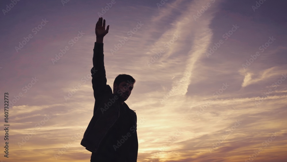 Fototapeta premium A man celebrating by raising his arms at sunset, symbolizing joy and freedom.
