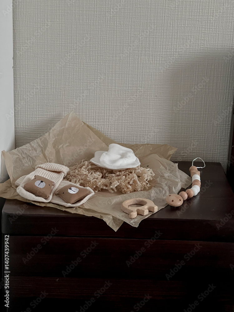 White scratches, beige socks with a bear, wooden beads, a wooden elephant teether are on the bedside table. Aesthetic minimalist baby fashion