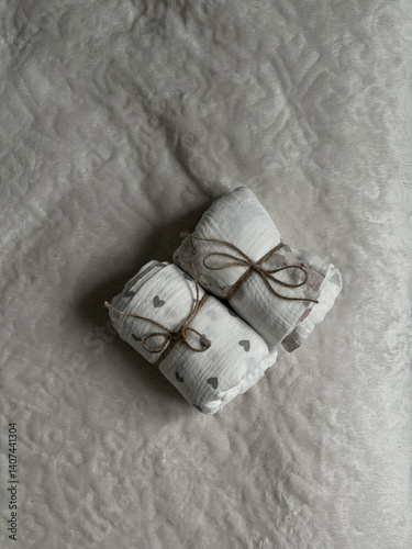 Two twisted muslin diapers and an elephant teether are lying on a milky-colored blanket. Children's fashion accessories