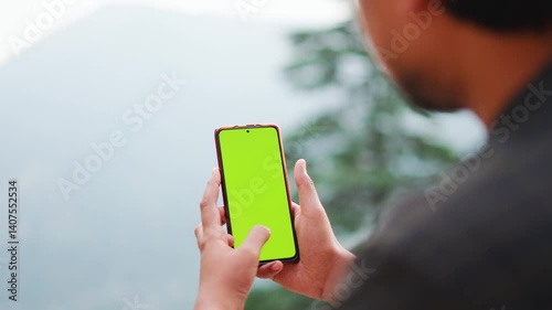 4K Closeup shot of hands of an Indian man holding mobile phone with green screen while standing outdoors. Chroma Key Mockup. Vertical green screen on mobile phone. Unknown person hold mobile phone.
