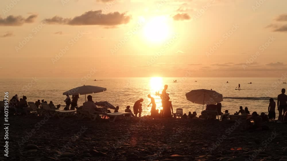 Peaceful evening on a pebble beach with people relaxing and enjoying the sunset by the sea. Calm summer vibes and warm pastel colors Peaceful evening on a pebble beach with people relaxing and enjoying the sunset by the sea. Calm summer vibes and warm pastel colors