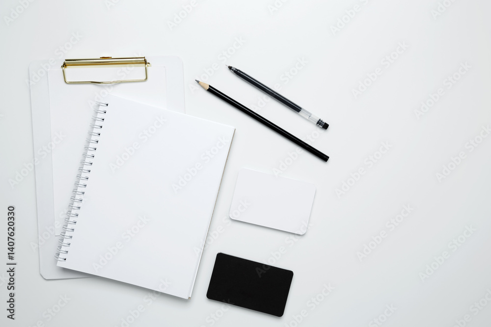 On a white background, an empty mock up notebook and clipboard, white and black cards, monochrome stationery items arranged neatly