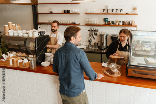 A view from the back of a White man aged 30, ordering some coffee from a mid-20s, overweight White female barista, as they stand inside a cozy coffee shop