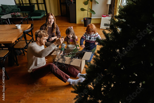 Fotografi A White adult man, his wife, daughter, and son are preparing Christmas decorations by untangling Christmas lights, while getting ready to decorate their Christmas tree in the cozy living room