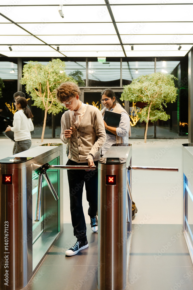 Diverse adult employees, including a White man and an Indian woman, enter a modern office through a turnstile with access cards indoors in a contemporary business environment.
