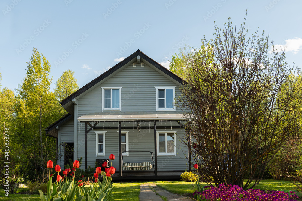 Contemporary wooden house have nice landscaping, with shrubs, green lawn and spring flowers. Traditional russian dacha in Moscow region. Outdoors. Backyard and traditional relax gardening.