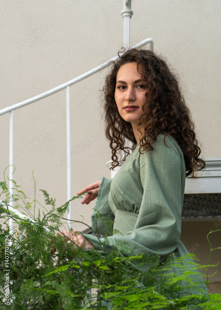 Pretty young woman standing on white staircase surrounded by lush green plants, creating natural atmosphere with touch of elegance and serenity. Pretty young woman standing on white staircase surrounded by lush green plants, creating natural atmosphere with touch of elegance and serenity.