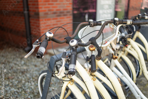 close-up view of bicycle handlebars at a bike-sharing station. The image highlights the details of the bicycle's design, showing the handlebars, grips, and lights. The background features a modern