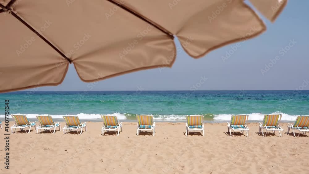 Tranquil sandy beach scene with sunshade overlooking rows of lounge chairs and gentle waves