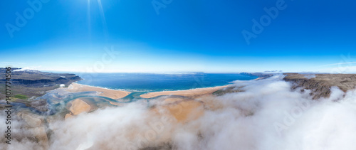 Obraz na płótnie Aerial view of Rauðasandur, Iceland, where golden sands meet turquoise waters, framed by dramatic cliffs and low-hanging clouds under a radiant blue sky. w salonie