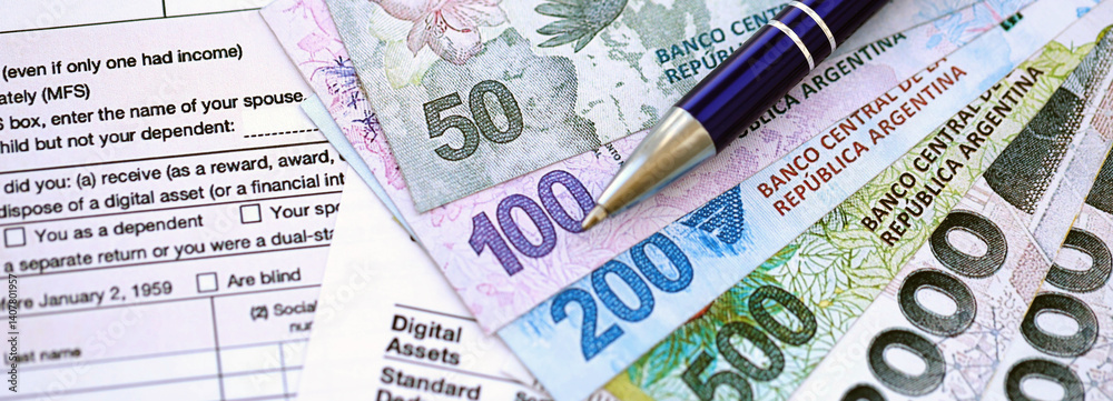 Argentine pesos money bills in big amount lies on table with pen and tax forms close up Argentine pesos money bills in big amount lies on table with pen and tax forms close up