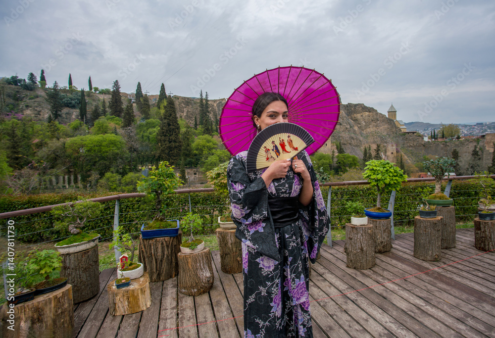 Beautiful young woman in Japanese kimono and close face with fan on holiday of cherry blossom