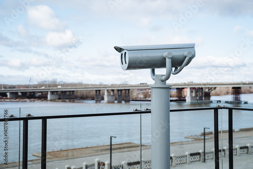 A security camera is mounted high atop a pole, carefully positioned to overlook a flowing river, ensuring constant surveillance of the area to enhance safety and security