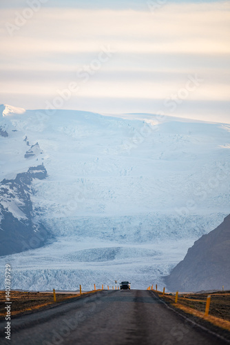 Obraz na płótnie A long empty road leads toward a majestic glacier-covered mountain in Iceland, under a soft pastel sky at sunrise. A breathtaking view of nature's raw beauty and endless adventure. w salonie