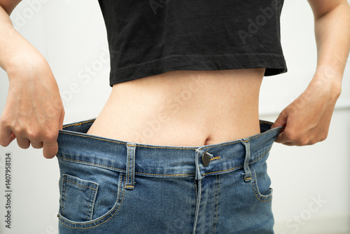 Young Asian woman losing weight wearing loose pants in oversize jeans.