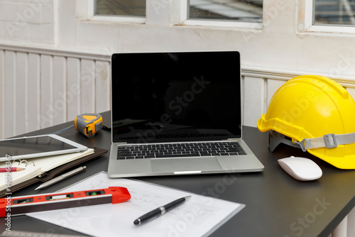 Wallpaper Mural A laptop with a blank screen sits beside a yellow hard hat on a desk, suggesting a blend of technology and construction or engineering. Torontodigital.ca
