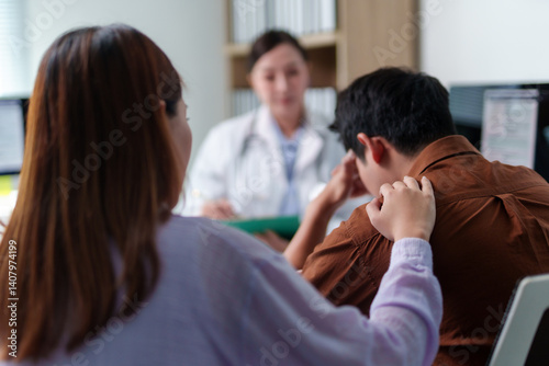 Asian woman comforting her sad husband while receiving bad news from doctor during medical consultation in hospital office