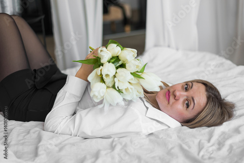 Young woman lying with tulips on white bed