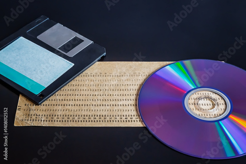 An old punch card, computer floppy disk, and compact disc on a dark background, showcasing outdated technology, 20th-century technology, early computer data, and an old archive.