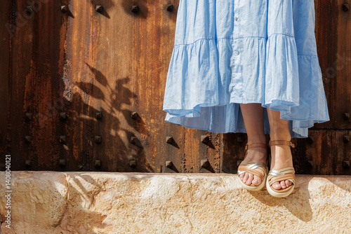 Close-up of a young woman's feet in sandals, resting on the step of a village gate on her vacation trip.