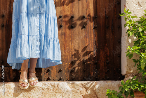 Close-up of a young woman's feet in sandals, resting on the step of a village gate on her vacation trip.