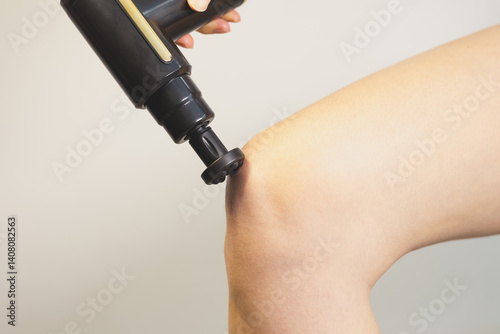 Obraz na płótnie Woman doing massage her knee with percussion massage gun. Physiotherapy, muscle recovery, self-massage tool. Healthcare. Close up. w salonie