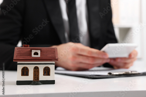 House figure and real estate agent with calculator at white table in office, selective focus. Home appraisal