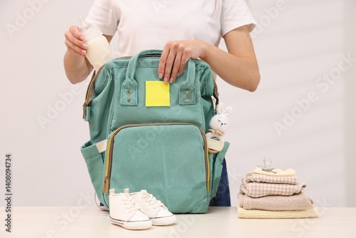 Mother packing baby's stuff into bag at white table, closeup