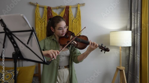 Young woman playing violin at home by sheet music, focused on learning music. Violin student rehearsing classical music in a professional study session