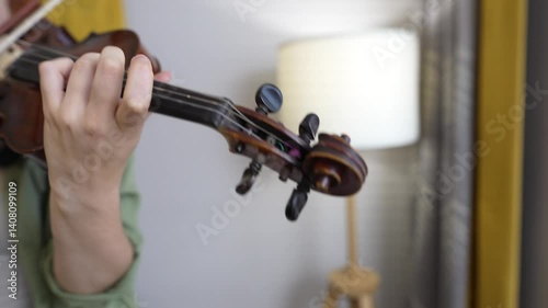 A woman hand moves along the neck of the violin, pinching the strings and chords. Playing the violin at home, close-up