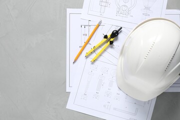 Different engineering drawings, hard hat, pencil and divider on grey table, flat lay. Space for text
