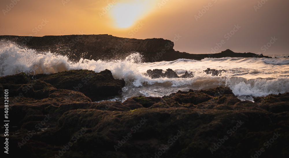 Obraz premium Dramatic waves crashing against rocky shore at sunset on north beach, Essaouira, Morocco