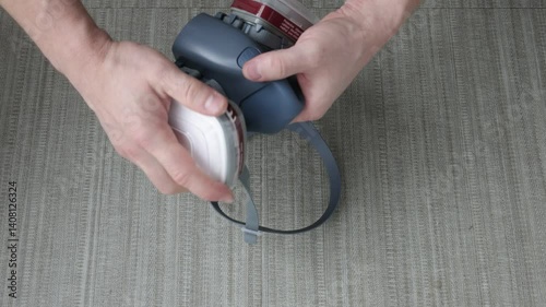 Man’s hands inserting a filter into a protective respirator mask on a gray surface, close-up view.