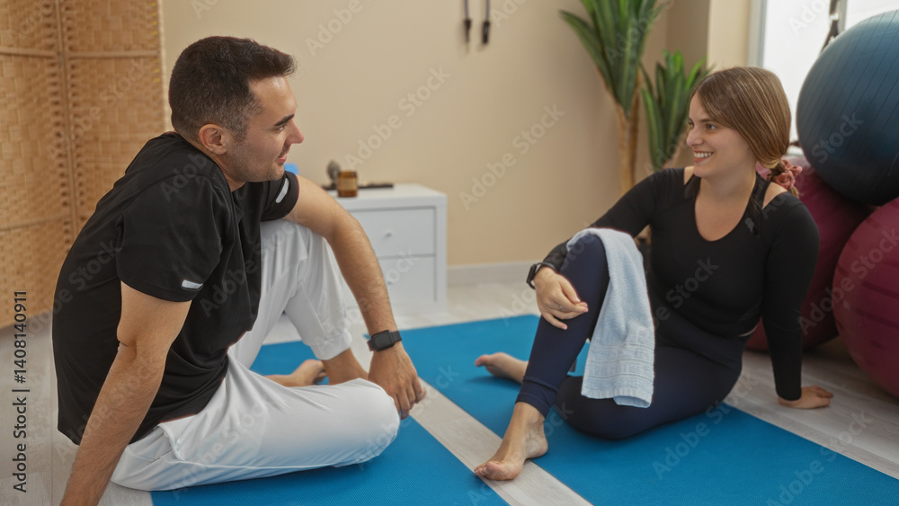 Obraz premium Man and woman enjoying a friendly conversation on yoga mats in a gym, highlighting a warm relationship in an indoor sports setting.