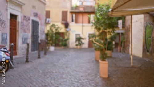 Photography Blurred image of a charming cobblestone street in rome, italy with historic buildings, vibrant graffiti, and potted plants creating a serene outdoor atmosphere