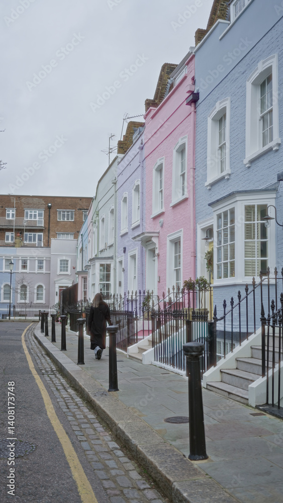 Woman walking down chelsea street in london with colorful houses lining the path under a cloudy sky.