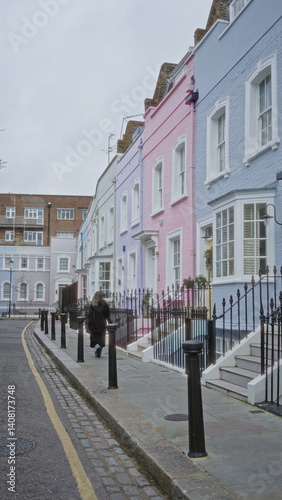 Obraz na płótnie Woman walking down chelsea street in london with colorful houses lining the path under a cloudy sky. w salonie