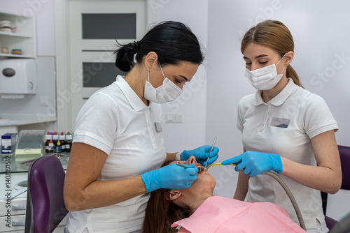 female patient being examined and treated by female dentist and an assistant in dental clinic.