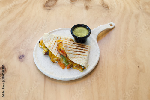Obraz na płótnie A plate of food with a tortilla wrap and a side of guacamole. The plate is on a wooden table w salonie