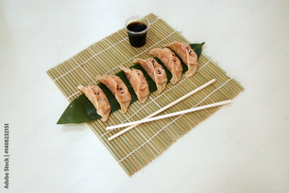 A plate of dumplings with chopsticks on a bamboo mat. The dumplings are arranged in a row and are covered with a leaf