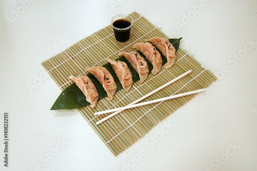 Obraz na płótnie A plate of dumplings with chopsticks on a bamboo mat. The dumplings are arranged in a row and are covered with a leaf w salonie