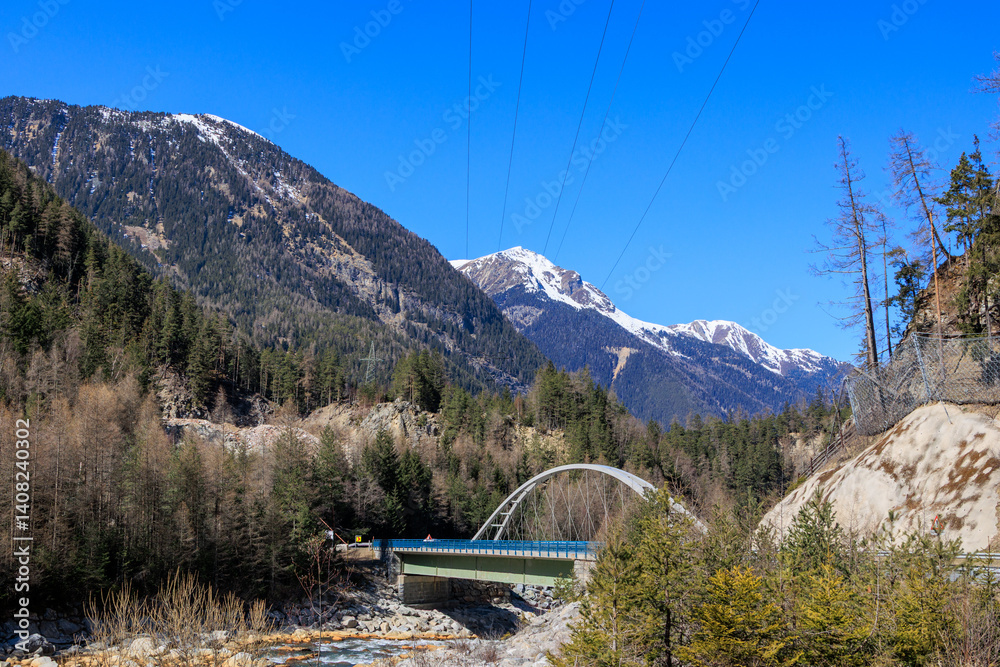 Mountain bridge crossing alpine river in early spring landscape..